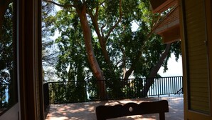 Un balcon avec un banc en bois, donnant sur une zone pavée agrémentée d’arbres et bordée d’une rambarde.