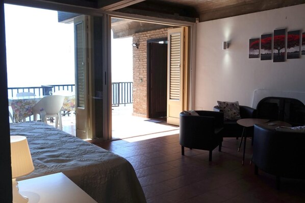 A room with a bed, two chairs, a small table, and a balcony with a railing.