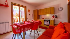 A compact kitchen with wooden cabinets, a dining table set for four, and a red couch. - Happy Guest Apartments Mountain Panorama Borno (BORNO)