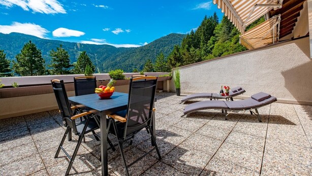 A terrace with a table and chairs, a lounge area with sun loungers, and a view of mountains. - Happy Guest Apartments Mountain Panorama Borno (BORNO)