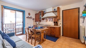Une cuisine compacte avec des meubles en bois, une table à manger agrémentée de sets de table bleus et une porte coulissante à cadre bleu donnant sur un balcon.