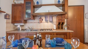 Une cuisine avec des meubles de rangement en bois, une cuisinière et une table à manger agrémentée de verres et d’assiettes bleus.