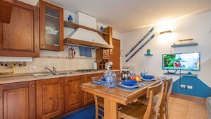 Une cuisine avec des meubles de rangement en bois, une table à manger dressée avec de l’assiette bleue, et un téléviseur fixé au mur.