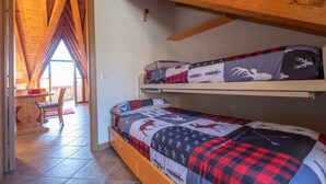 A dormitory room with two bunk beds, a wooden ceiling, and a view through a window.