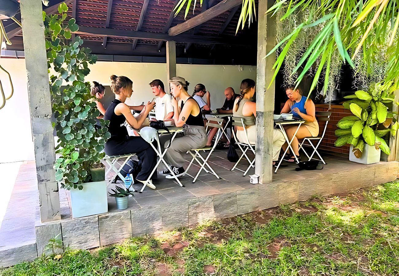A covered outdoor seating area with tables and chairs, surrounded by greenery and plants.