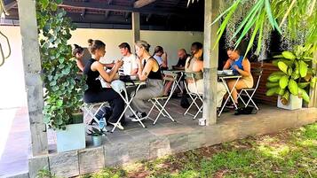 A covered outdoor seating area with tables and chairs, surrounded by greenery and plants.