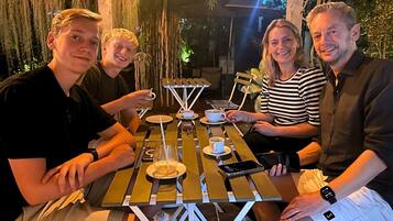 Un grupo de personas sentadas en una mesa al aire libre con una taza de café, un teléfono inteligente y un reloj sobre la mesa.