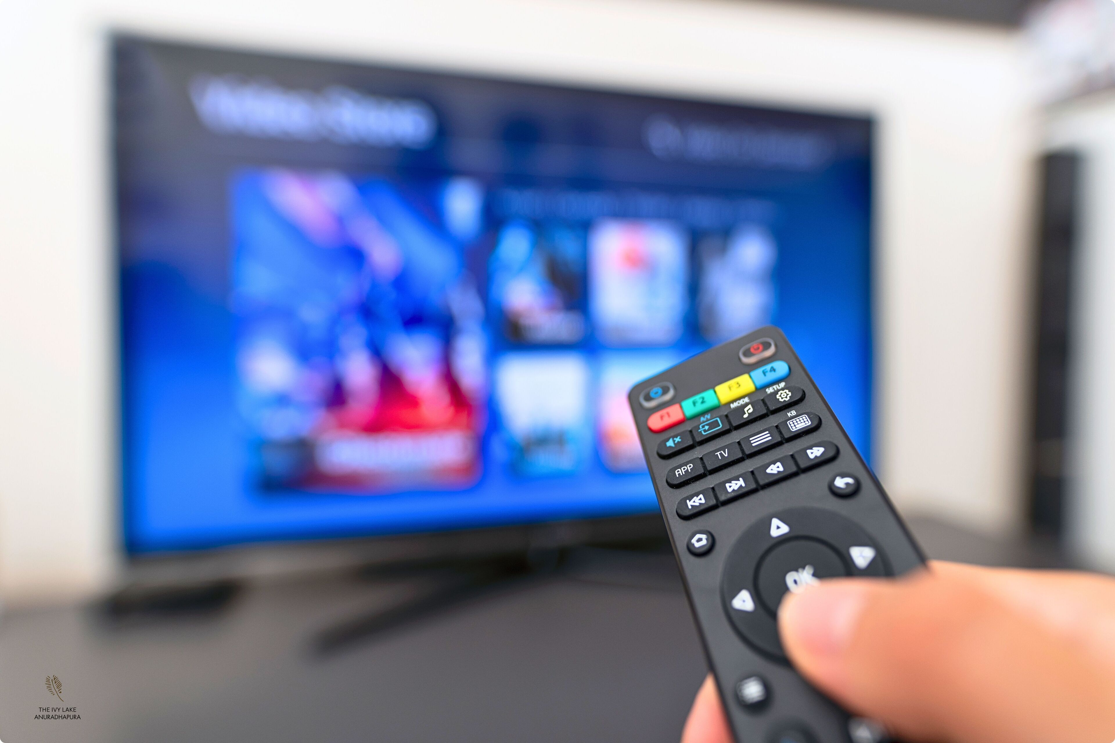 Eine Hand hält eine Fernbedienung vor einem Fernseher.