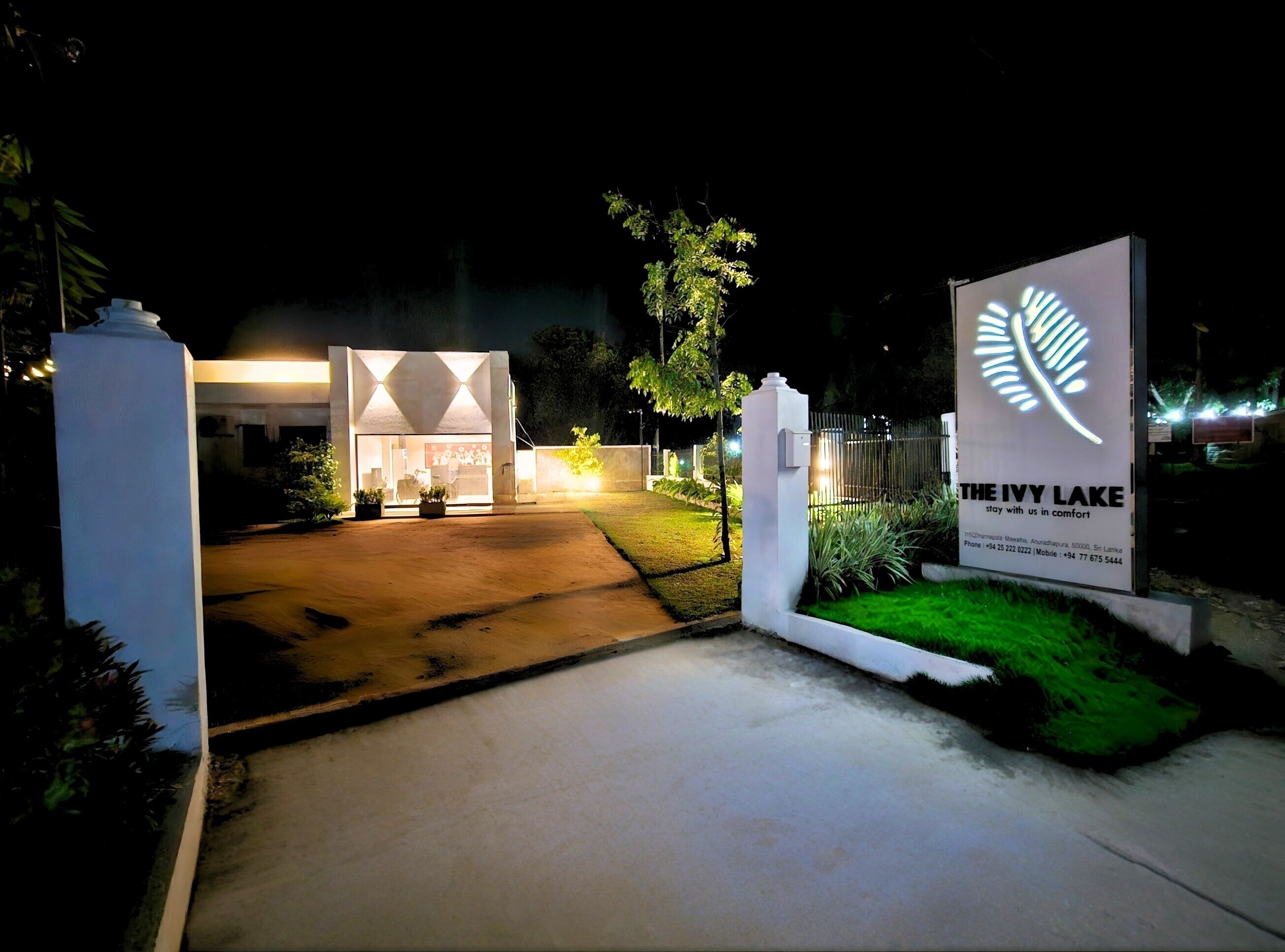 Entrada de hotel con un camino bien iluminado, un cartel anunciando 'The Ivy Lake', y un edificio moderno con diseños geométricos.