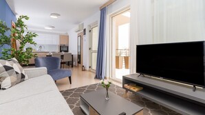 A modern living room with a sofa, a TV, a coffee table, and a dining area in the background. - Domus Lauri Palace Resort terrace 4 perosons (Umag)