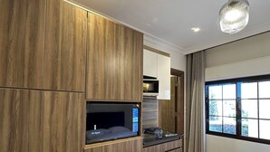 Une chambre d’hôtel moderne avec une armoire en bois, un coin cuisine intégré, un lit et une grande fenêtre.