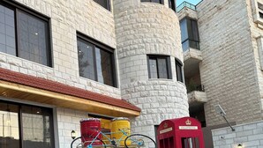 Une voiture jaune, modèle ancien, est garée devant un immeuble à la façade en pierre, à côté d’une cabine téléphonique rouge.
