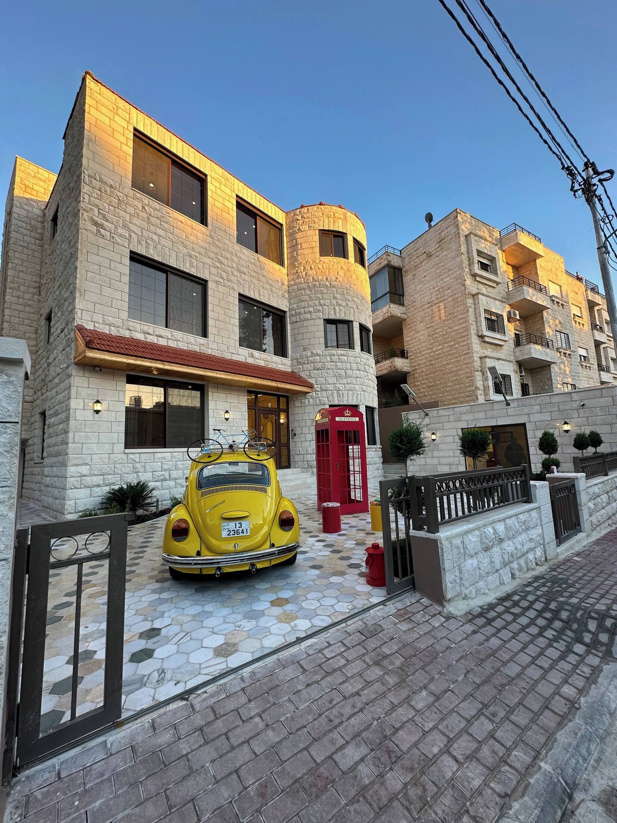 A building with a stone facade, a red telephone booth, and a vintage yellow car parked in front.
