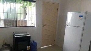 A kitchen with a gas stove, a refrigerator, and a window with bars. - Casa das Flores (Rio das Ostras)