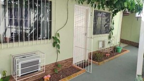 A house with a covered porch, a small garden area with plants, and a window with a metal grill. - Casa das Flores (Rio das Ostras)