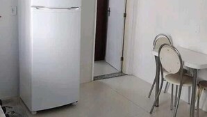 A room with a white refrigerator, a dining table with four chairs, and a door leading to another room. - Casa das Flores (Rio das Ostras)