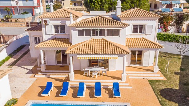 A two-story house with a swimming pool, blue lounge chairs, and a covered patio area.
