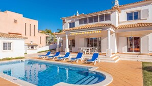 A two-story house with a swimming pool, outdoor seating, and a patio area.