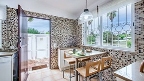 Una cocina con salpicadero de azulejos, un comedor con mesa y sillas, y una ventana con vistas a la vegetación.