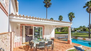 Un patio al aire libre con piscina, zona de estar cubierta y mesa de comedor con sillas.