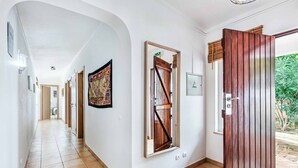 Un pasillo con suelo de baldosas, una puerta de madera con diseño de panel vertical y un aplique en la pared.