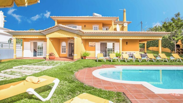 Een gele villa met zwembad, terras en tuin.