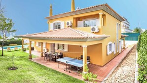 Een huis met twee verdiepingen, een terras, airconditionings en een zwembad op de achtergrond.