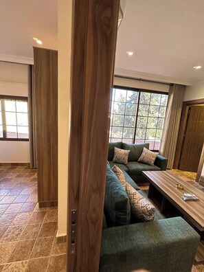 A modern living room with a sectional sofa, a wooden coffee table, and a large window with a view of trees.