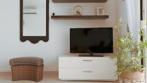 A living room with a flat-screen TV, a white cabinet, a wicker ottoman, and a mirror on the wall. - Magnifique Studio vue mer (Saint martin)
