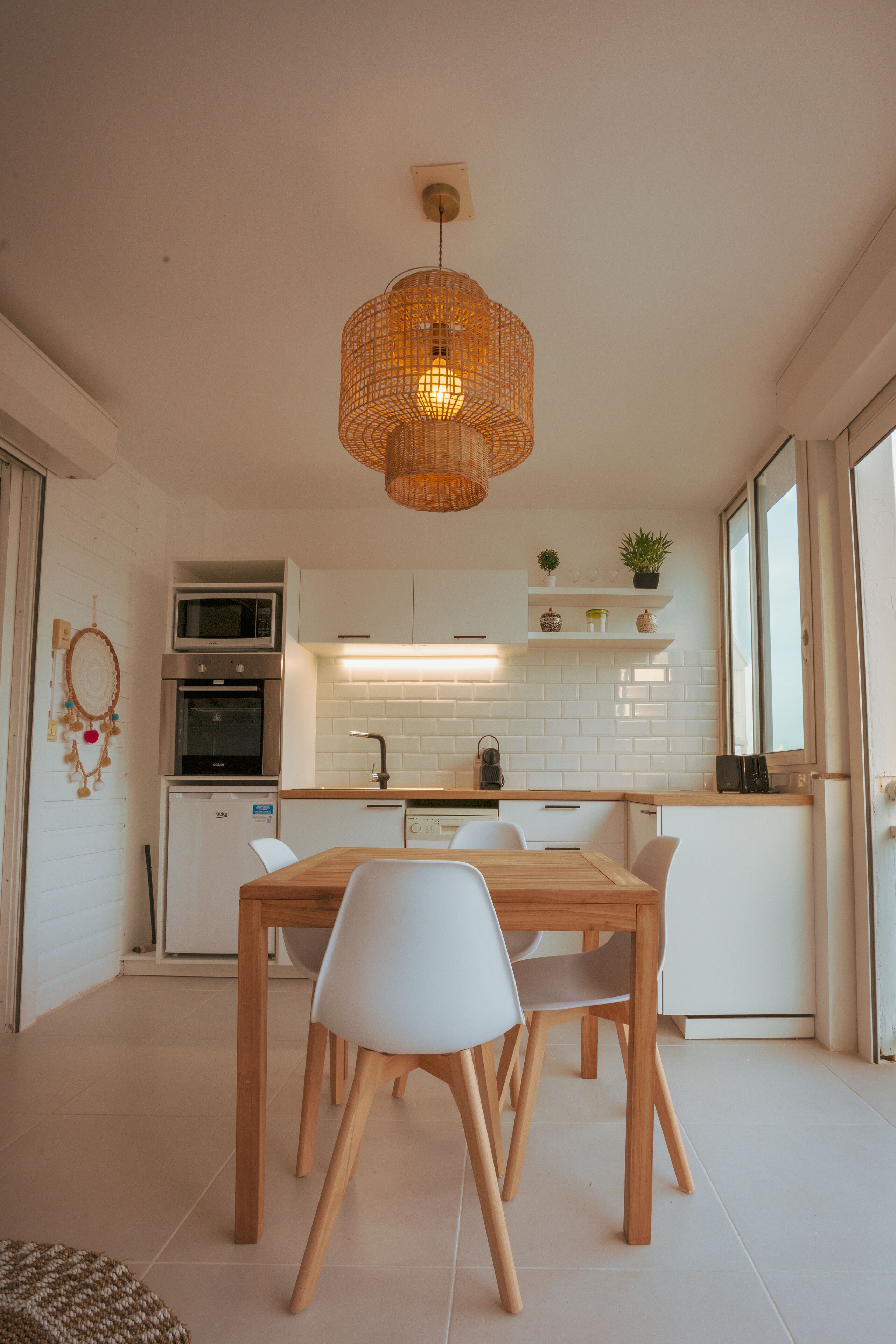 A compact kitchen with white cabinets, a microwave, oven, and a wooden dining table with chairs. - Magnifique Studio vue mer (Saint martin)