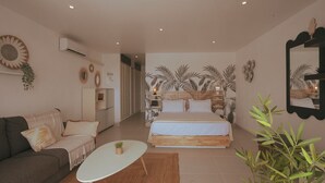 A modern bedroom with a large bed, a sofa, a small table, and a mirror. - Magnifique Studio vue mer (Saint martin)