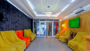 A lobby with yellow sofas, a television, and a ceiling with recessed lighting. - Appart Hotel Les orchidees (Cotonou)