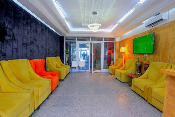 A lobby with yellow sofas, a television, and a ceiling with recessed lighting. - Appart Hotel Les orchidees (Cotonou)