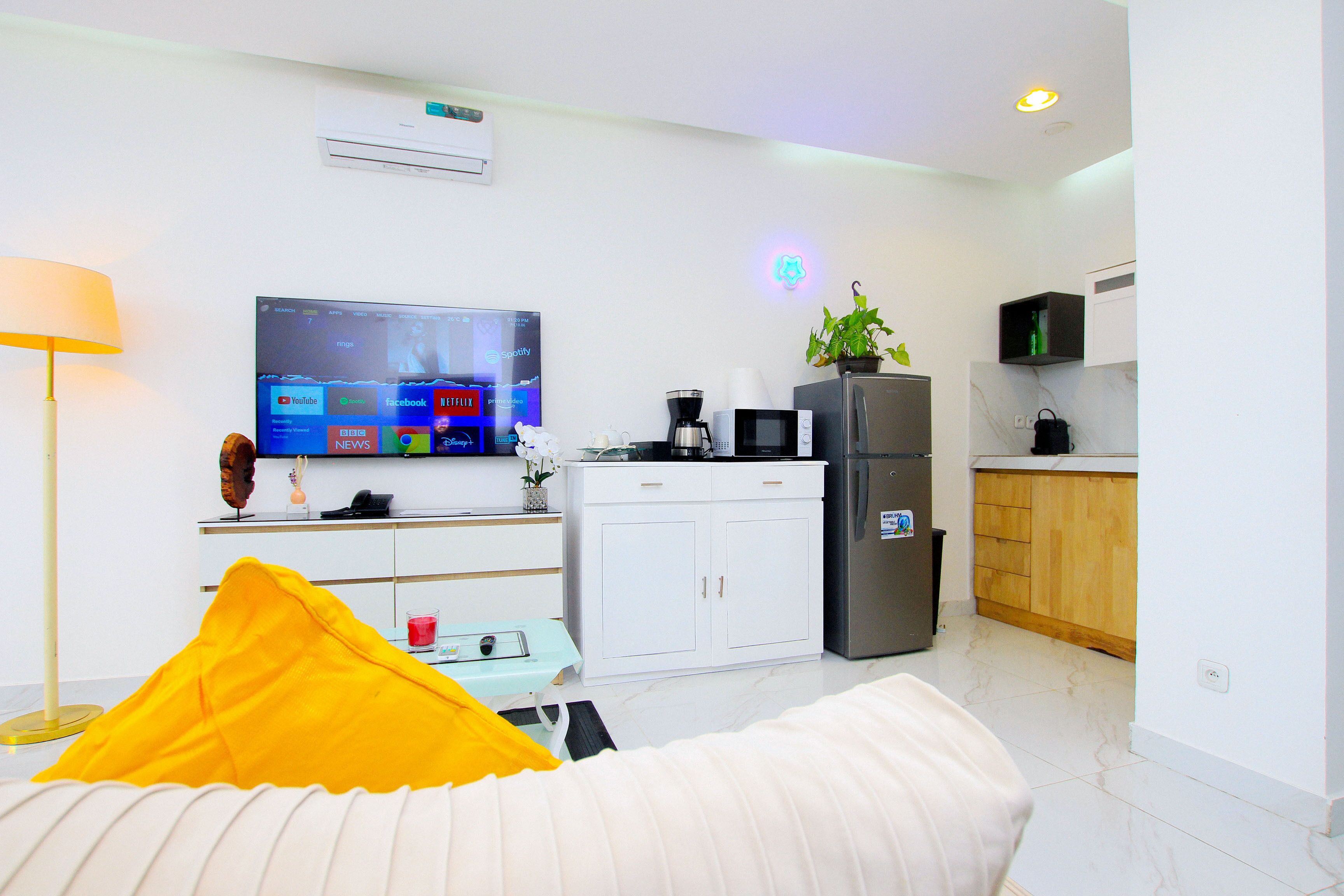 Una sala de estar moderna con un televisor de pantalla plana, una cafetera y una cocina con armarios de madera y un refrigerador.