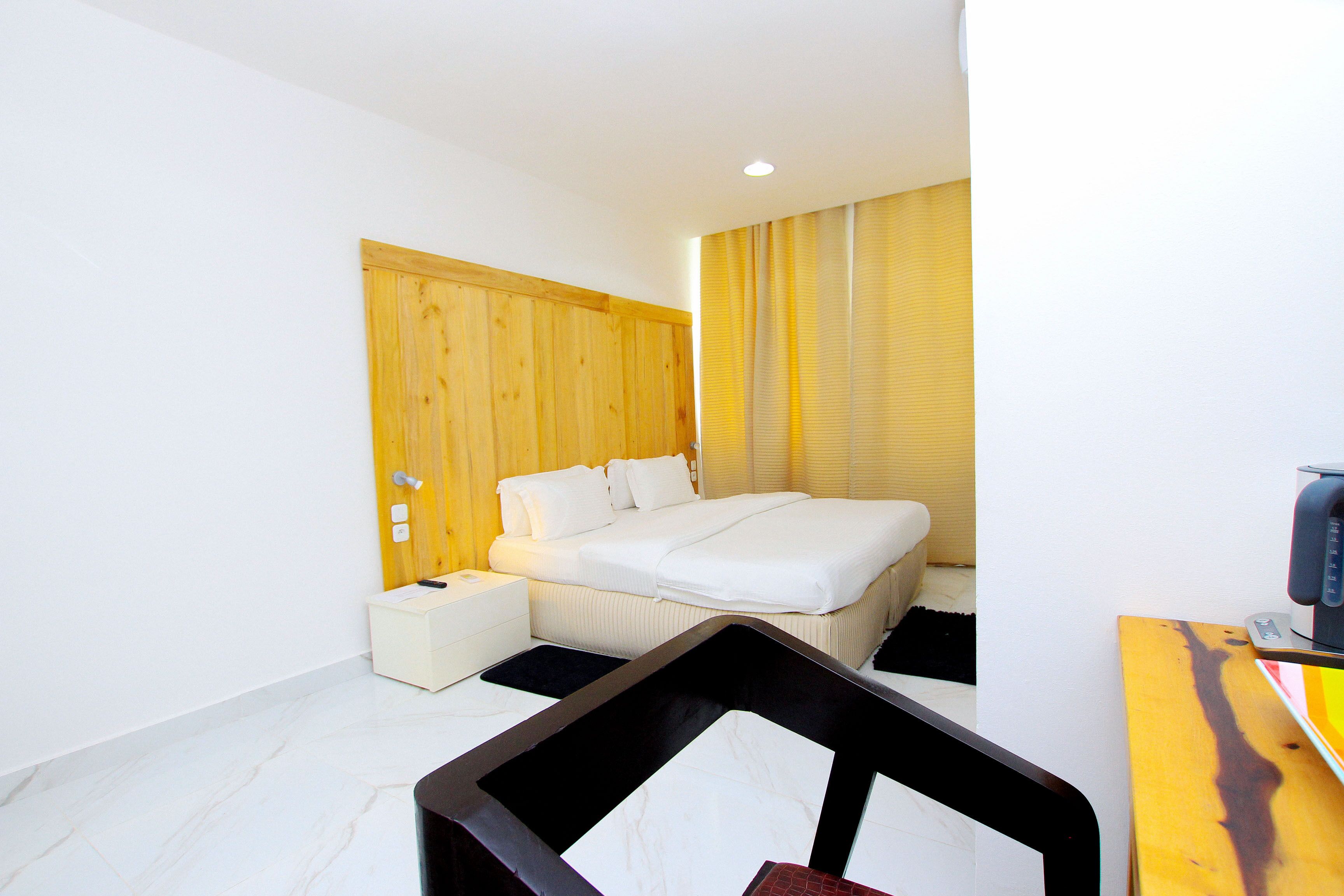 Una habitación de hotel moderna con una cama grande, cabecera de madera, una mesita de noche pequeña y un escritorio con una computadora.