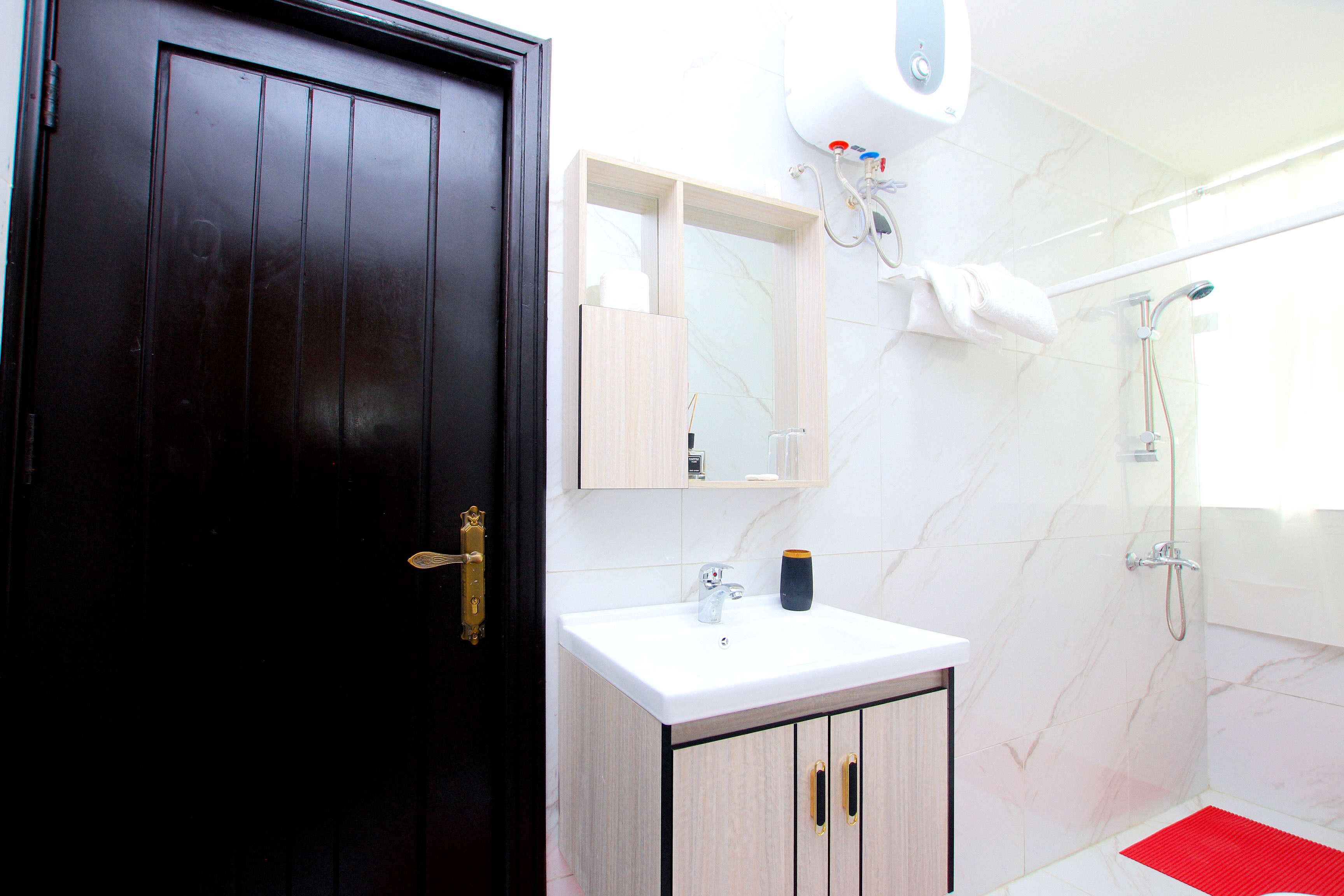 Un baño moderno con una puerta de madera oscura, un lavamanos blanco con un espejo encima, una toalla colgada en la pared y una zona de ducha.