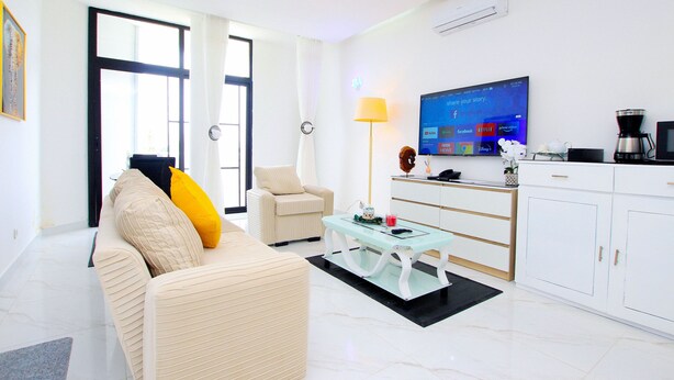 A modern living room with a sofa, armchair, coffee table, and a TV mounted on the wall. - Appart Hotel Les orchidees (Cotonou)
