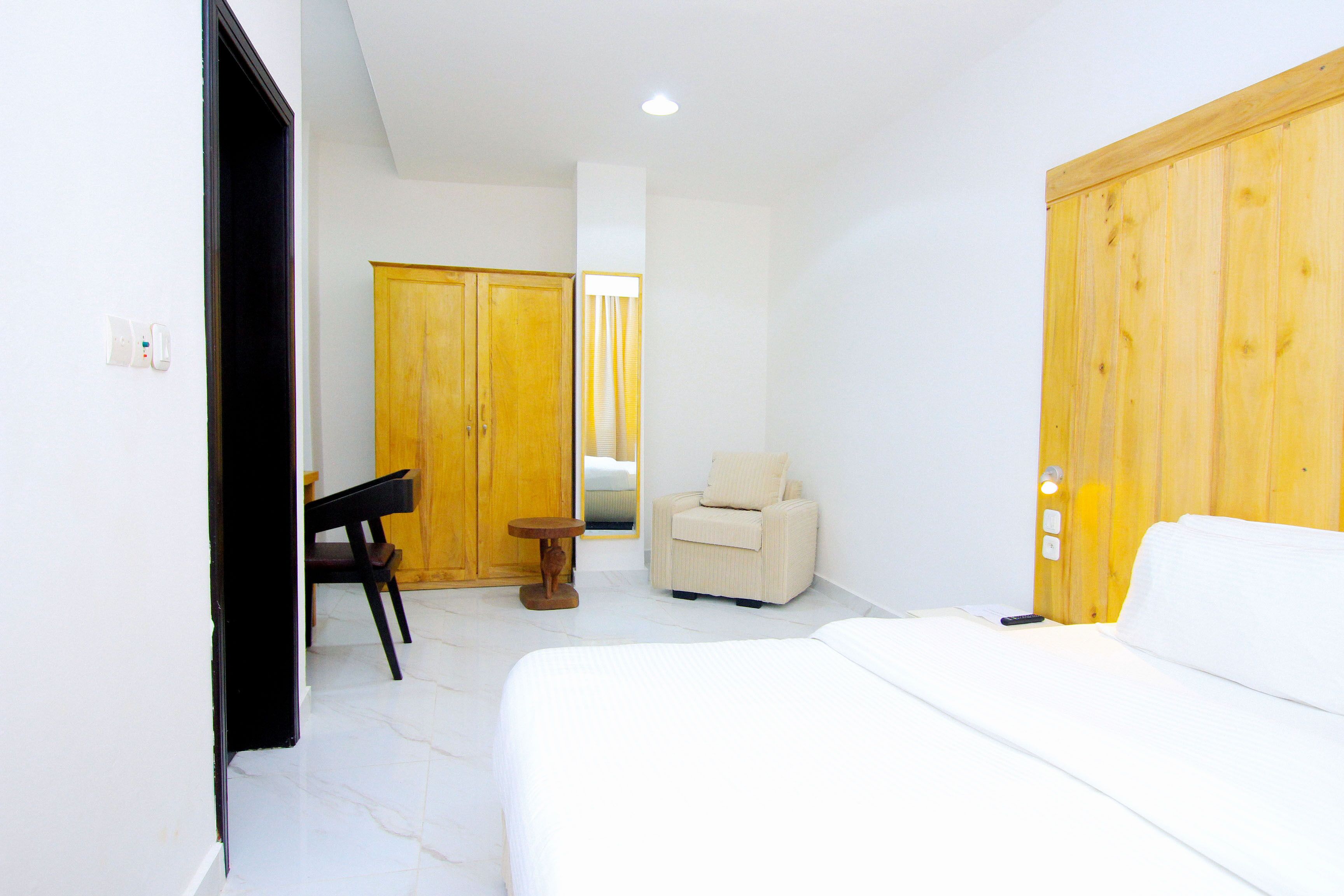 Una habitación de hotel con cama, una silla, una mesita pequeña y armarios de madera.
