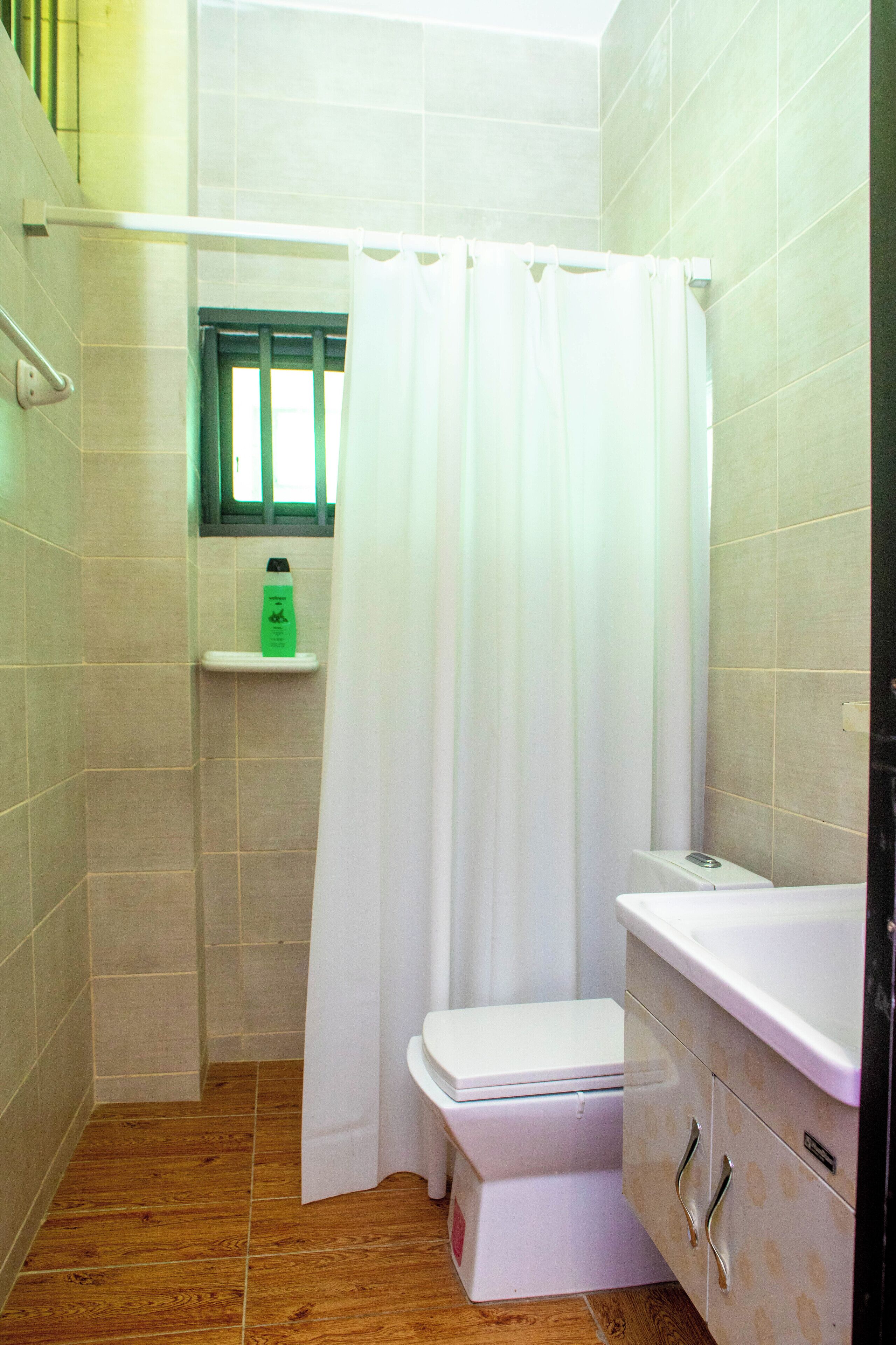 Un baño pequeño con inodoro, cortina de ducha y repisas con artículos de aseo.
