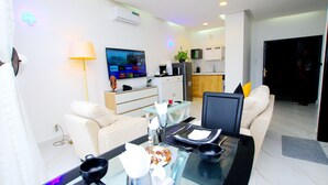 A modern living room with a glass dining table, white sofas, and a flat-screen TV mounted on the wall. - Appart Hotel Les orchidees (Cotonou)