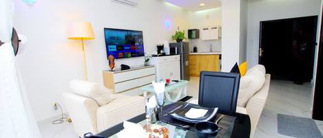 Una sala moderna con una mesa de comedor de cristal, sofás blancos y un televisor de pantalla plana montado en la pared.