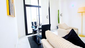A modern living room with a sofa, a dining table with chairs, and a large window with curtains. - Appart Hotel Les orchidees (Cotonou)