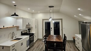 A modern kitchen with white cabinets, a wooden dining table, and a stainless steel refrigerator. - Cozy, private apt in small river town with short drive to city-border WI and IA. (Brownsville)