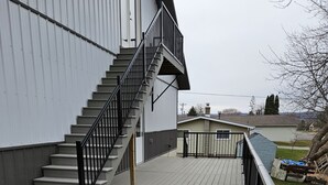 A wooden deck with a metal staircase leading to a building. - Cozy, private apt in small river town with short drive to city-border WI and IA. (Brownsville)