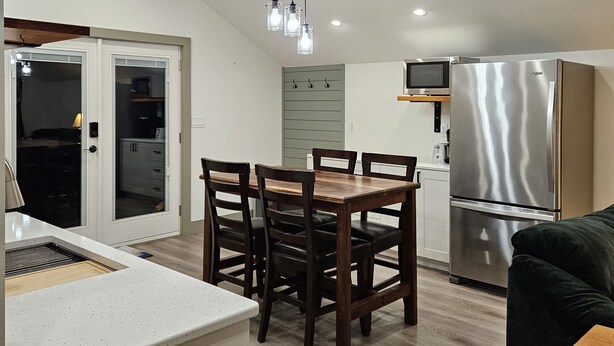 A modern kitchen with a dining area, featuring a stainless steel refrigerator, wooden chairs, and pendant lighting. - Cozy, private apt in small river town with short drive to city-border WI and IA. (Brownsville)