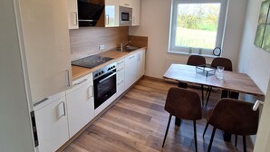 A modern kitchen with white cabinets, a wooden countertop, and a built-in oven. There is a dining area with a table and chairs, and a window providing a view of the outdoors.