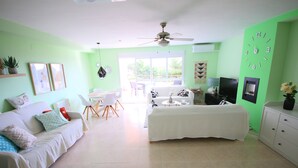 Un salon lumineux avec un canapé, un lit, une télévision et un ventilateur de plafond.