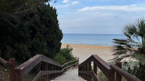 Un escalier en bois menant à une plage, avec un ciel dégagé.