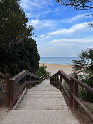 Un escalier en bois menant à une plage, avec un ciel dégagé.