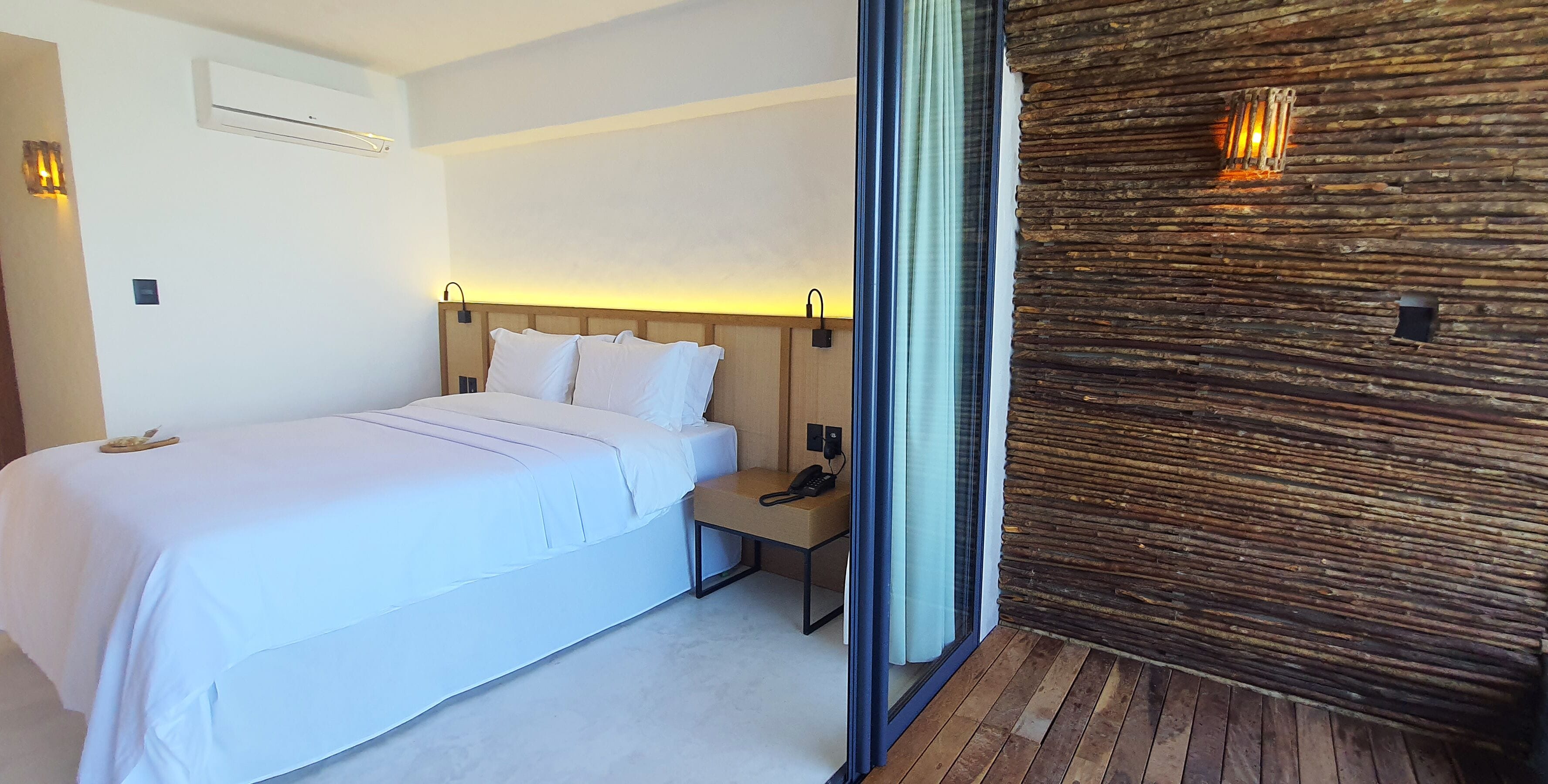 A modern hotel room with a large bed, a bedside table, a phone, and a wooden wall.